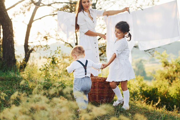 Ama de casa secando ropa Joven madre con su pequeña hija y su hijo está al aire libre en el bosque Hermoso sol