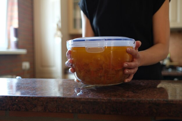 Ama de casa sosteniendo un recipiente de plástico con sopa en sus manos de cerca