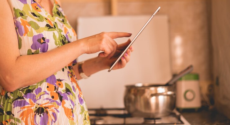 Foto ama de casa sosteniendo un teléfono inteligente o tableta para verificar el recibo mientras cocina en la cocina