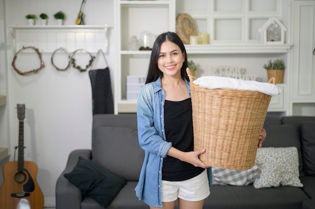 Un ama de llaves feliz lleva un cubo de paños para lavar la ropa en la casa.