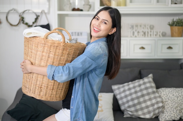 Un ama de llaves feliz lleva un cubo de paños para lavar la ropa en la casa.