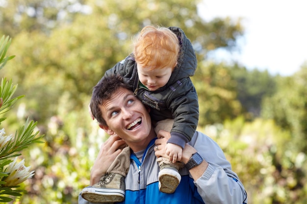 Ama la naturaleza al igual que su padre Un padre joven que lleva a su hijo pequeño sobre sus hombros