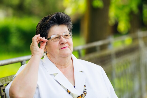 Amable anciana de blusa blanca sosteniendo sus lentes