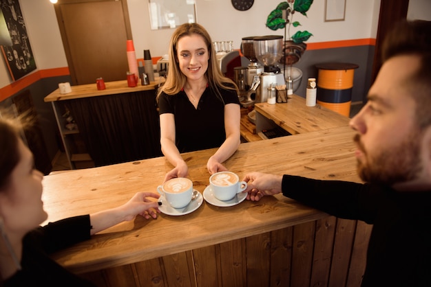 Un amable barman que sirve café expreso a los clientes en el interior de una moderna cafetería.