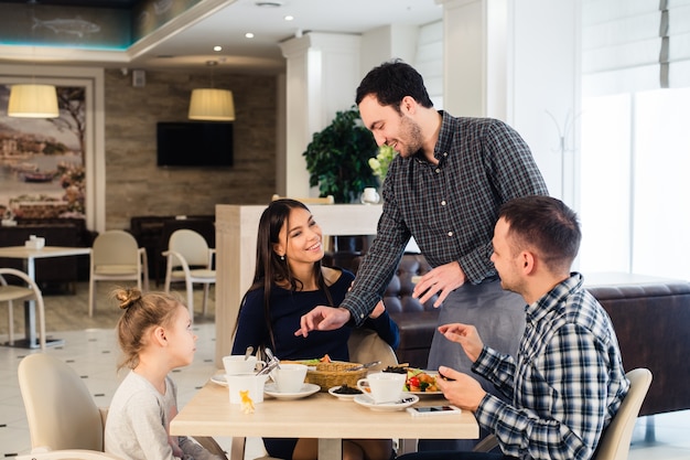 Amable camarero sonriente tomando orden en la mesa de la familia cenando juntos