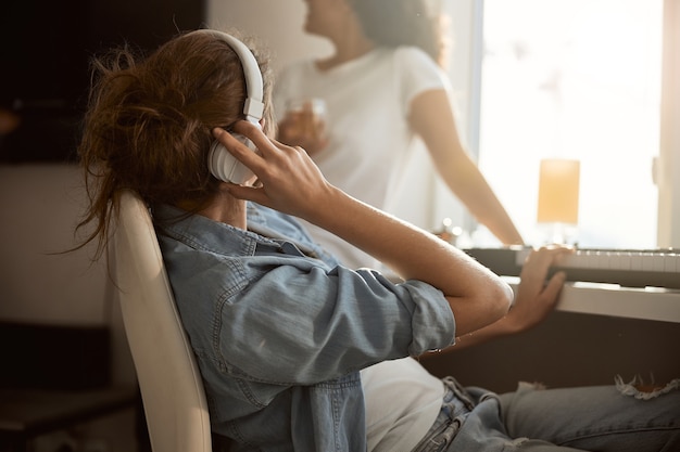 Amable compositor sentado cerca de su instrumento y con auriculares, mirando la ventana