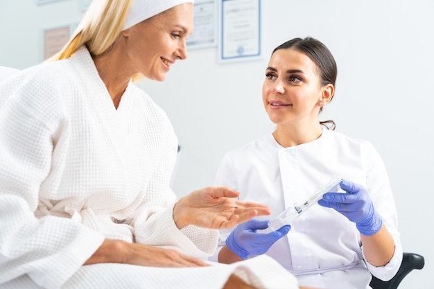 Amable dermatóloga joven demostrando un relleno dérmico a su cliente antes de un procedimiento cosmético