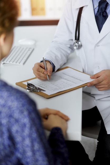 Amable doctor de barba roja y mujer paciente discutiendo el examen de salud actual mientras está sentado en una clínica soleada. Concepto de medicina.