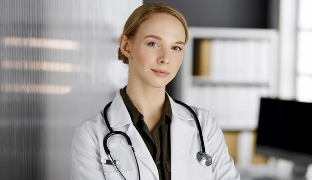 Amable doctora sonriente de pie en la clínica. Retrato de mujer médico amable. Perfecto servicio médico en el hospital.