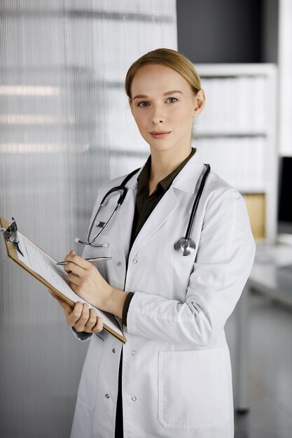 Amable doctora sonriente usando portapapeles en la clínica. Retrato de una mujer médica amigable en el trabajo. Servicio médico en el hospital. Concepto de medicina.