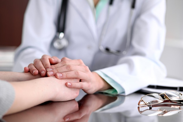 Foto la amable doctora sostiene la mano del paciente sentada en el escritorio para alentar, empatía, animar y apoyar durante el examen médico. disminución de malas noticias, compasión, confianza y ética conce