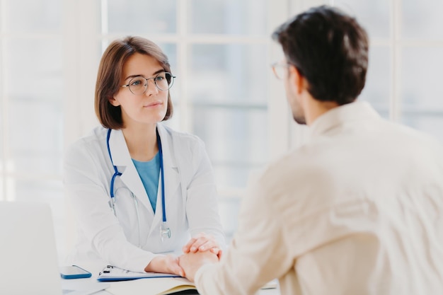 La amable doctora trata de ayudar al paciente a sostener sus manos, brinda una consulta útil y explica la información médica, hace que el examen de diagnóstico pose en la habitación del hospital.