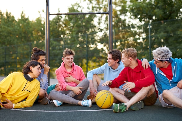 Amable equipo de chicos jóvenes sentados en el patio de baloncesto