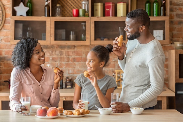 Amable familia afroamericana conversando durante el desayuno en la cocina, feliz ambiente acogedor, espacio de copia