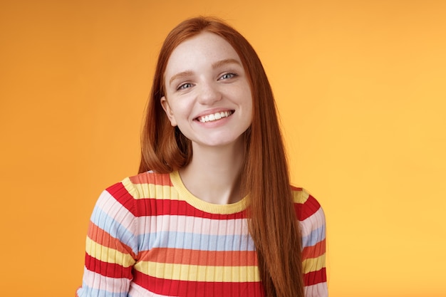 Amable femenino bonita pelirroja caucásica hermana sonriendo ampliamente tener perfecto estado de ánimo feliz hablando casualmente disfrutar de un buen día soleado de verano de pie fondo naranja encantado relajado