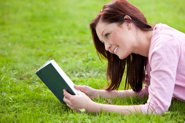Amable joven leyendo un libro tumbado en la hierba