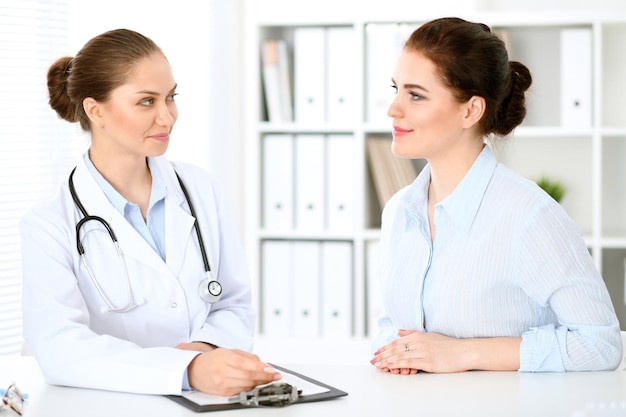 Amable médico sonriente y paciente sentado en la mesa. Muy buenas noticias y concepto de servicio médico de alto nivel.