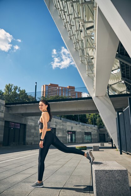 Amable mujer estirando su pierna mientras se prepara para correr a larga distancia