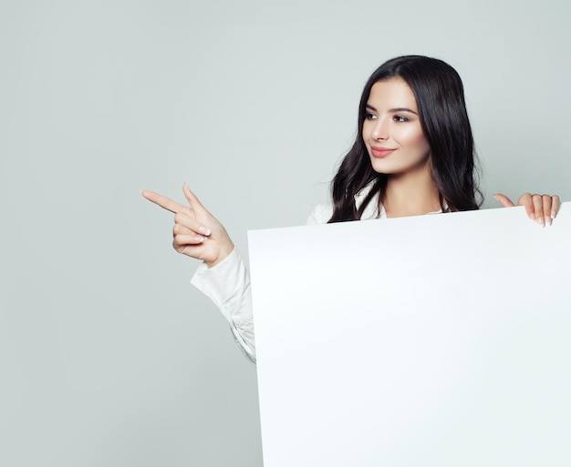 Amable mujer de negocios señalando con el dedo y mostrando un cartel con un espacio en blanco para publicidad o mensaje de texto en fondo blanco