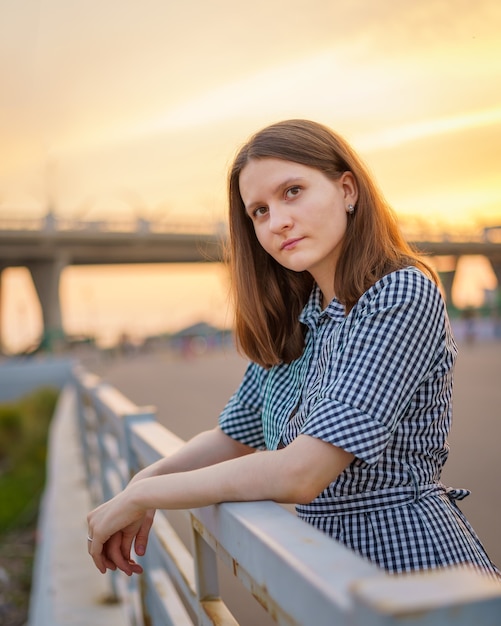 Amable rubia atractiva con el pelo largo al atardecer en el fondo del puente