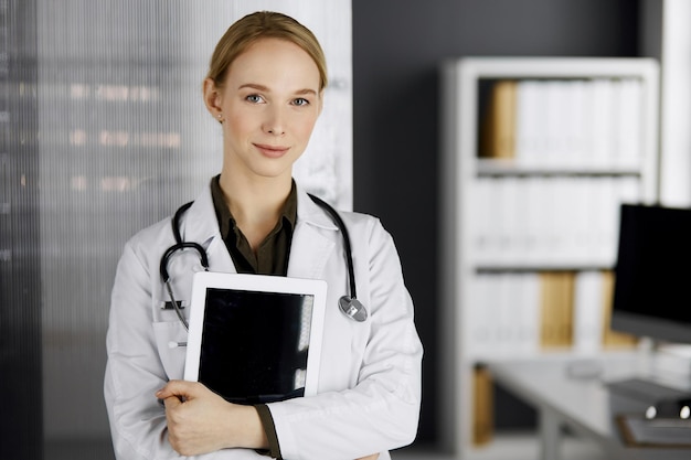 Amable y sonriente doctora usando una tableta en la clínica. Perfecto servicio médico en el hospital. Concepto de medicina.