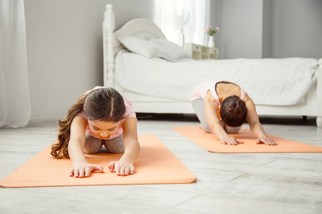 Amamos el deporte. Niña de cabello oscuro concentrada haciendo ejercicios mientras está acostada sobre la alfombra y su mamá haciendo ejercicio en el