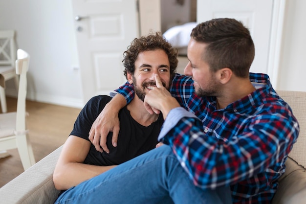 Amando a una pareja gay masculina del mismo sexo tumbada en el sofá en casa y relajándose abrazándose juntos