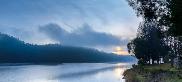 Amanecer cerca de la colina y el lago con árboles