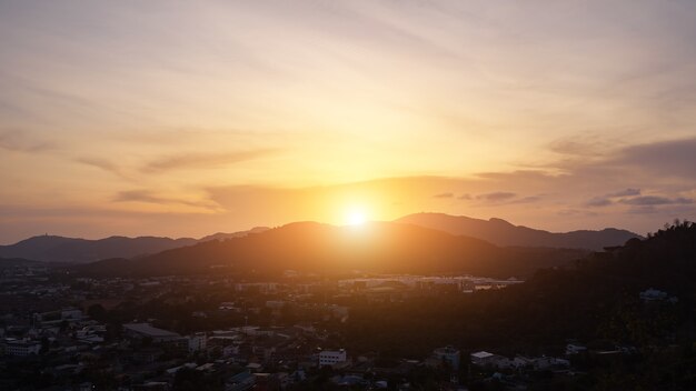 El amanecer entra en el atardecer sobre las colinas que rodean el valle con una pequeña ciudad y bosques en timelapse de país tropical