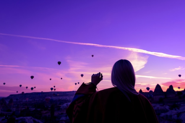 Amanecer mágico en Goreme Capadocia Turquía. Una niña en un cañón con ropas tradicionales rodeada de globos en los rayos del sol naciente