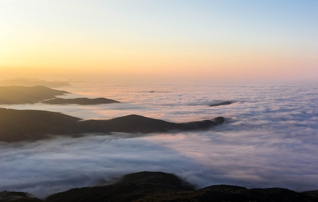 Amanecer en las montañas con nubes bajas. Montañas en capas en la niebla. Vista desde lo alto al valle.