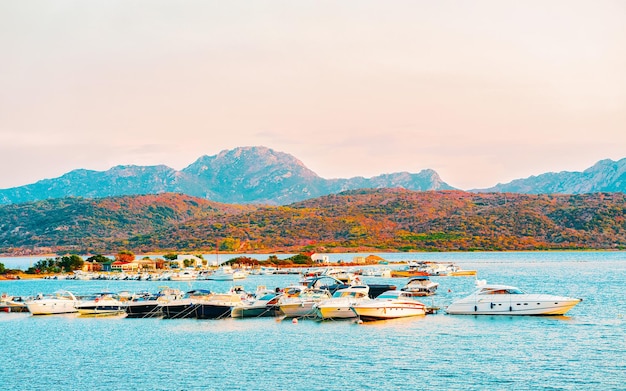 Amanecer o atardecer con yates en Porto Rotondo en Costa Smeralda en el mar Mediterráneo en Cerdeña, isla de Italia. Barco en Cerdeña en verano. Paisaje de la provincia de Olbia. Técnica mixta.