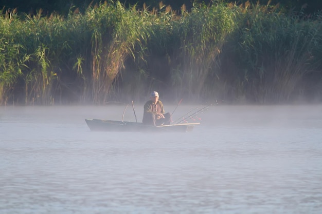 Amanecer en el río el vapor se eleva sobre el agua Un pescador se sienta en un bote y pesca