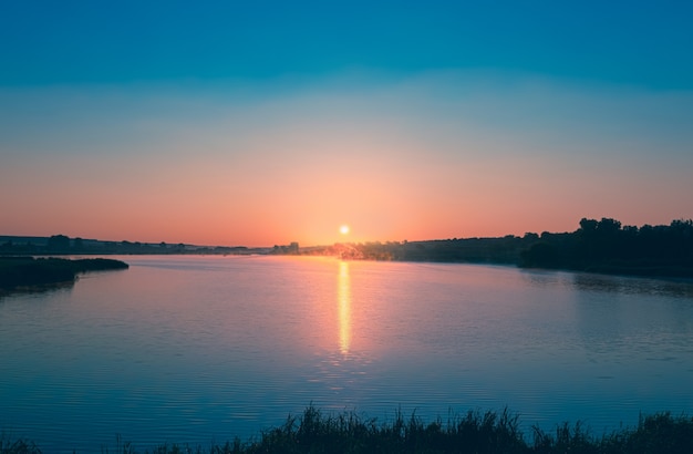 Amanecer rosa el sol se eleva sobre las tranquilas aguas azules del estanque una franja de luz solar se refleja en el ...