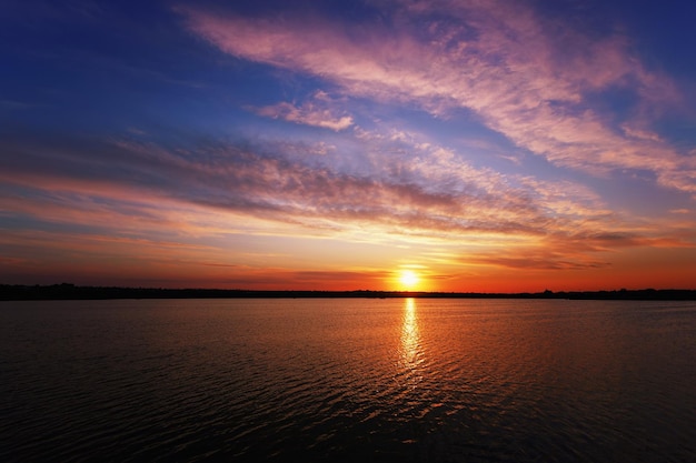 Amanecer sobre el lago con reflejo de nubes y sol.