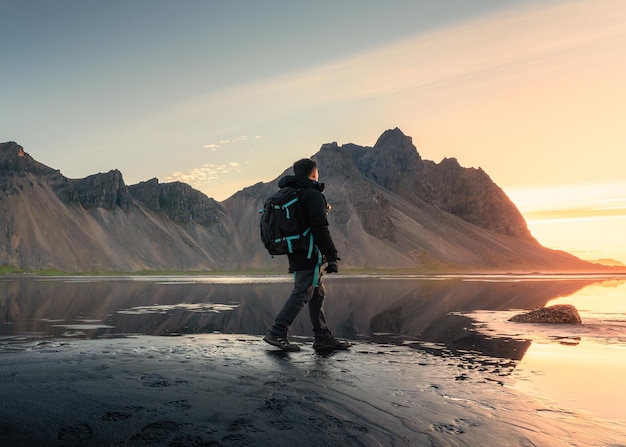 Amanecer sobre la montaña Vestrahorn y un mochilero caminando sobre una playa de arena negra en Stokksnes, en el sureste de Islandia