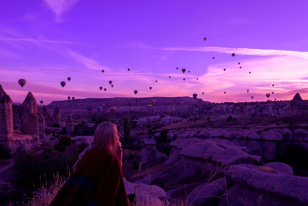 Amanhecer mágico em Goreme Capadócia Turquia. uma garota em um desfiladeiro com roupas tradicionais, cercada por balões sob os raios do sol nascente