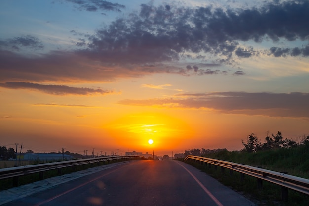 Amanhecer na estrada. O sol brilhante nasce contra o céu laranja. Paisagem de manhã.