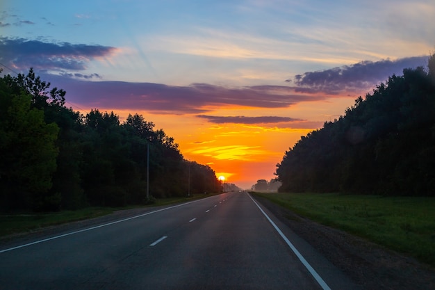 Amanhecer na estrada. o sol nasce contra o fundo do céu com nuvens, ao redor da floresta. paisagem de manhã.