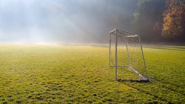 Amanhecer no campo de futebol amador. Parque infantil do jogo de futebol na manhã de nevoeiro de outono.