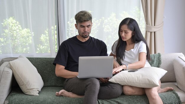 Amante casal asiático relaxando no sofá e navegando na internet com computador portátil