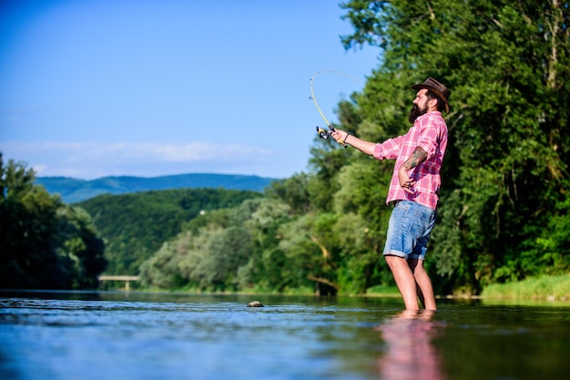 Amante da natureza hipster pescando com colher de pescador de sucesso no lago água pesca com mosca passatempo Atividade de pesca de verão pesca desportiva relaxa na natureza homem barbudo maduro com peixe na vara