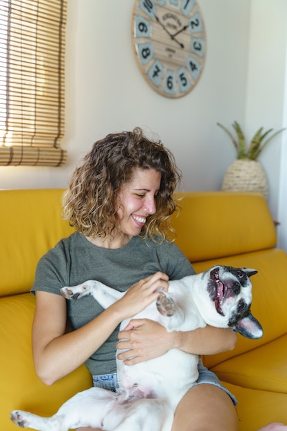 Foto amante de cachorro mulher com bulldog em casa no sofá. visão vertical de mulher fazendo cócegas em seu cachorro.