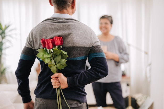Amante de casal adulto sênior fofo homem gentil surpresa dando flores rosas para aniversário de casamento ou dia dos namorados para sua esposa em casa