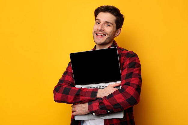 Amante de gadgets animado homem abraçando laptop no estúdio