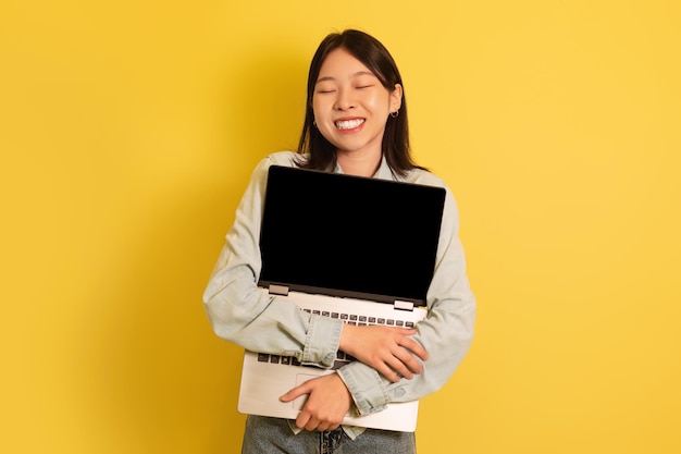 Amante de tecnologia alegre jovem asiática abraçando laptop com maquete de tela em branco para