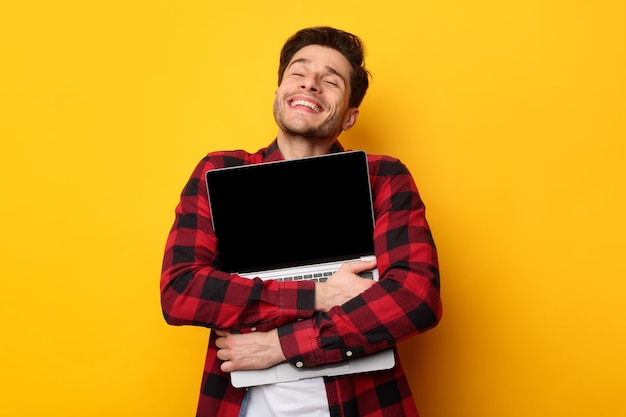 Amante de tecnologia animado homem abraçando laptop no estúdio
