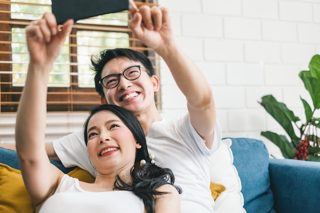 Amante do jovem casal asiático tirando selfie pelo celular em casa relaxa e estilo de vida em casa conceito