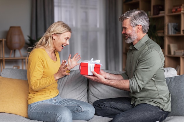 Amante esposo de mediana edad sorprendiendo a su esposa con un regalo en casa