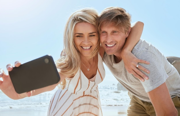 Amante jovem casal tomando selfie com telefone enquanto desfruta de um dia na praia sorrindo e abraçando Romântico marido e mulher mostrando carinho e tirando fotos para mídias sociais durante as férias